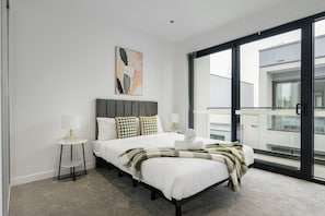 Une chambre à coucher moderne avec un grand lit, une table de chevet, une lampe et une vue sur l’extérieur.