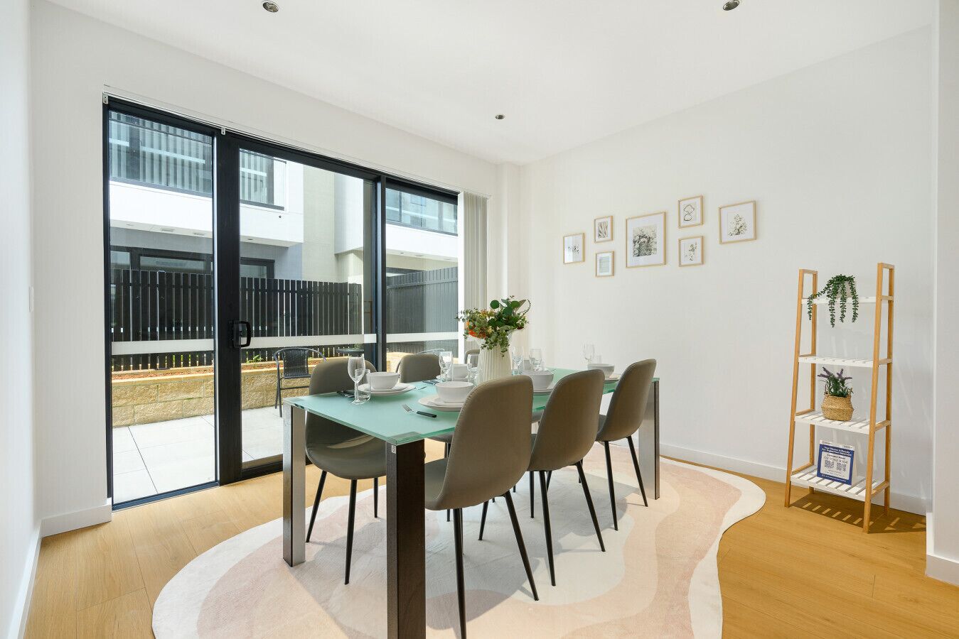 A dining area with a table set for four, chairs, a vase with flowers, and a plant on a shelf.