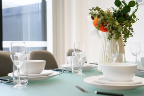 A dining table set with white plates, bowls, and clear wine glasses, with a vase of green foliage and orange flowers on the table. - Brand New Family Home for 10 | Boxhill (Box Hill)