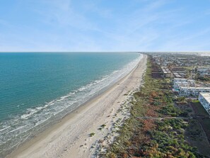 Luftaufnahme einer Küstenstadt mit Strand, Gebäuden und Grünflächen.