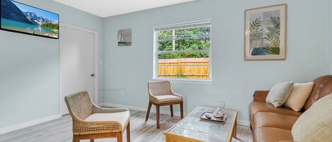 A living room with a sofa, two chairs, a coffee table, a TV, and a window with a view of greenery.