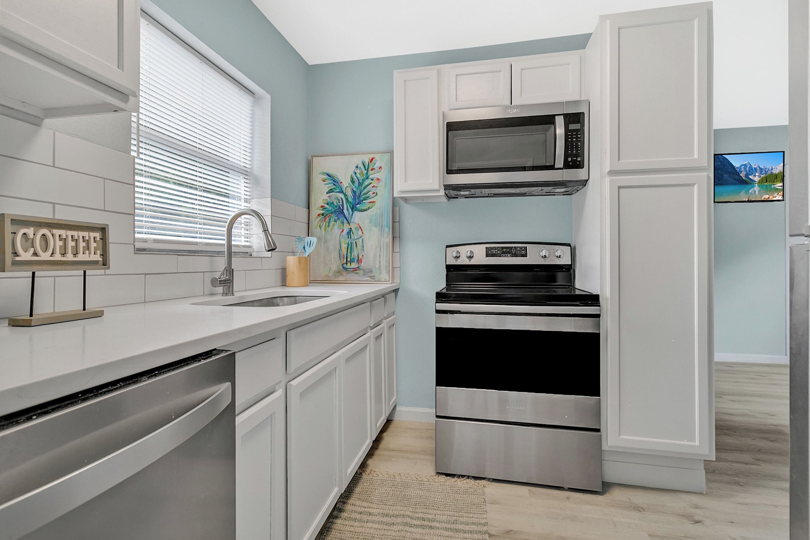 A modern kitchen with white cabinetry, a stainless steel stove, a microwave, and a sink with a faucet.