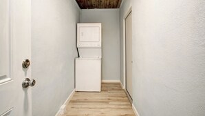 Ein schmaler Korridor mit Holzboden, einer weißen Tür links und einem weißen Kühlschrank rechts.
