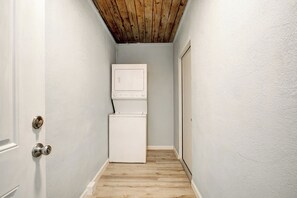 Ein schmaler Korridor mit Holzboden, einer weißen Tür links und einem weißen Kühlschrank rechts.