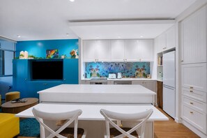 A modern kitchen with white cabinets, a blue accent wall, and a large island with chairs. - The Fishbowl - 1Bed-1Bath-1Car-Pool (Bulimba)