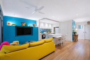 Ein modernes Wohnzimmer mit einem gelben Sofa, einem Flachbildfernseher und einem Deckenventilator.