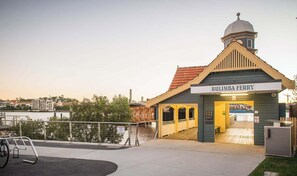 A building with a sign reading 'BULIMBA FERRY' and a dock extending into a body of water. - The Fishbowl - 1Bed-1Bath-1Car-Pool (Bulimba)