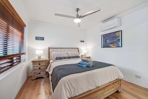 Ein Schlafzimmer mit Bett, Nachttischen, Deckenventilator, Klimaanlage und Bildern an der Wand.