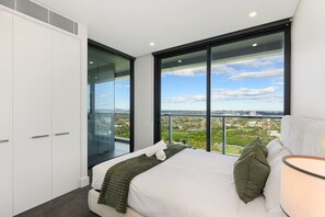 Een slaapkamer met een groot bed, uitzicht op een stadsbeeld en een schuifdeur naar een balkon.