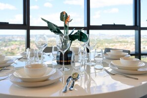 A dining table set with plates, bowls, and wine glasses, with a decorative vase in the center. - Spacious High-Rise 4Br Apartment | Olympic Park (Sydney Olympic Park)