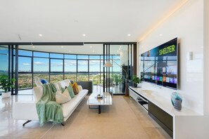 Ein modernes Wohnzimmer mit großem Fenster, einer Couch, einem Couchtisch und einem flachbildfernseher an der Wand.
