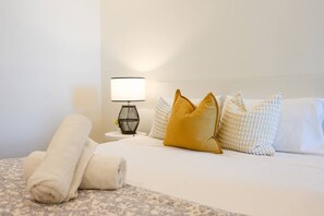 A neatly made bed with white linens, a single yellow pillow, and a rolled towel on a patterned carpet. - Spacious High-Rise 4Br Apartment | Olympic Park (Sydney Olympic Park)
