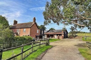 A rural property with a brick house, a wooden fence, and a dirt path leading to a barn.