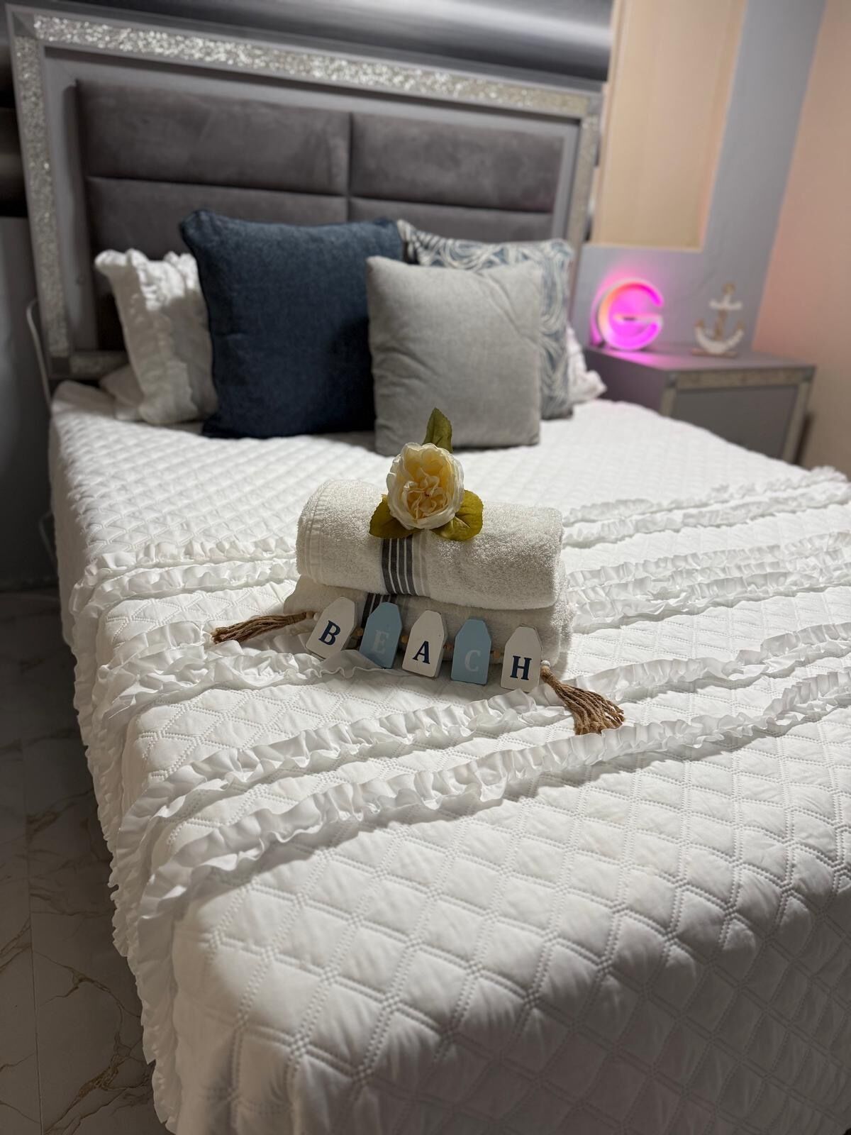 Een net opgemaakt bed met een decoratieve kussenschikking en een klein bloemstuk.