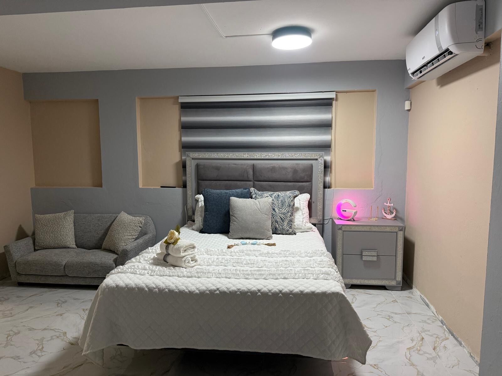 A bedroom with a bed, bedside table, nightstand, and an air conditioning unit.