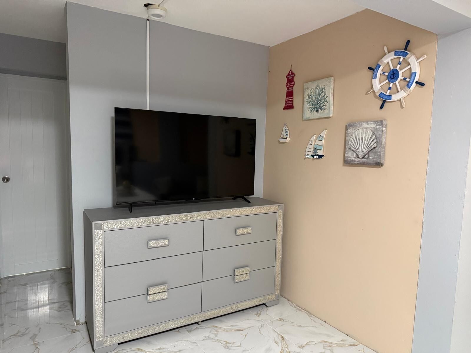 Een kamer met een televisie op een kast, een plafondlamp en muurdecoraties met een nautisch thema.