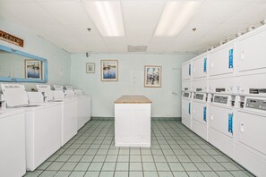 A laundromat with rows of washing machines, a mirror, and artwork on the walls. - Oceanfront 5th-Floor Condo at Beach Colony - Lazy River, Pools, Sleeps 6 (Myrtle Beach)