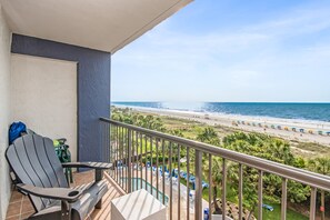 Ein Balkon mit Blick auf einen Strand, ein Schwimmbad und Strandstühle.