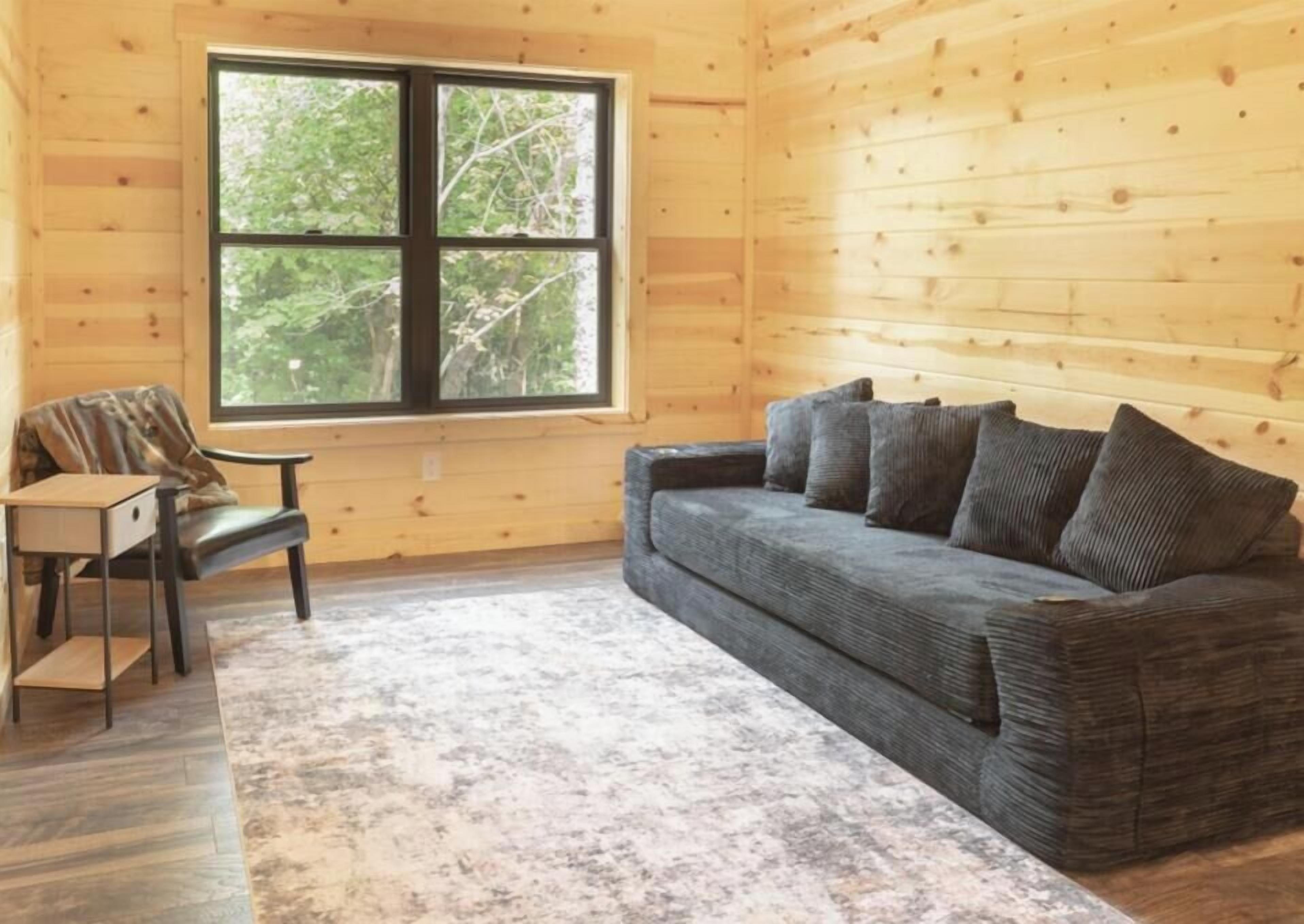 Ein Zimmer mit Holzvertäfelung, einer Couch mit Kissen, einem kleinen Tisch und einem Fenster mit Blick auf Bäume.