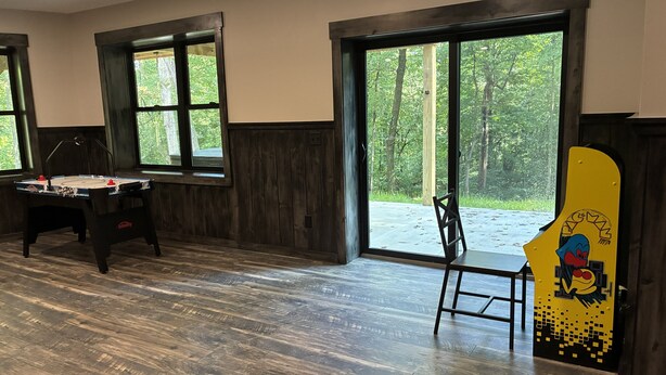A room with a foosball table, a chair, and a large window with a view of trees. - The Wooded Obsidian Overlook cabin, with hot tub, games, and close to everything (Logan)