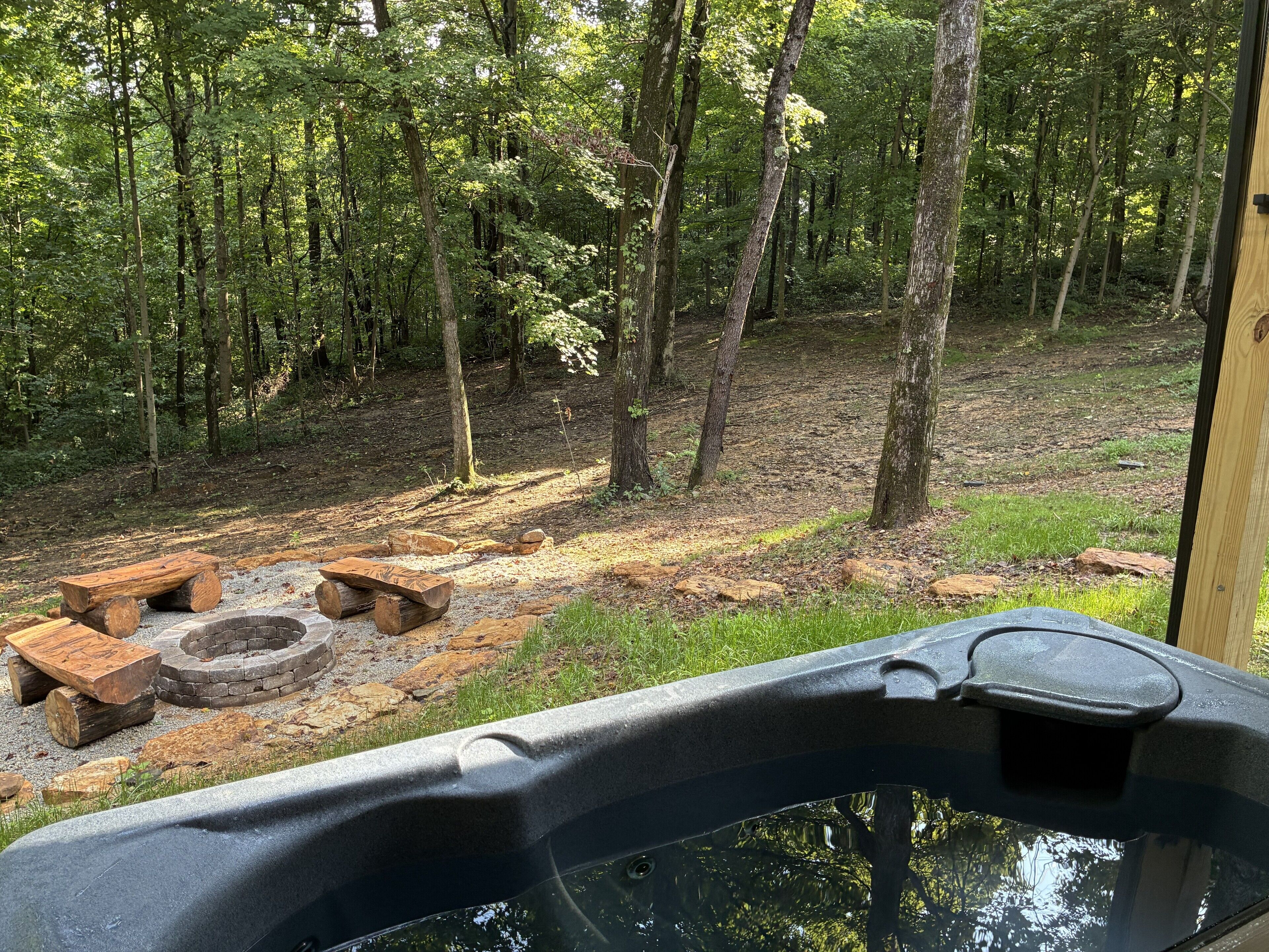 A hot tub with a stone fire pit and a wooden bench in a forested area.