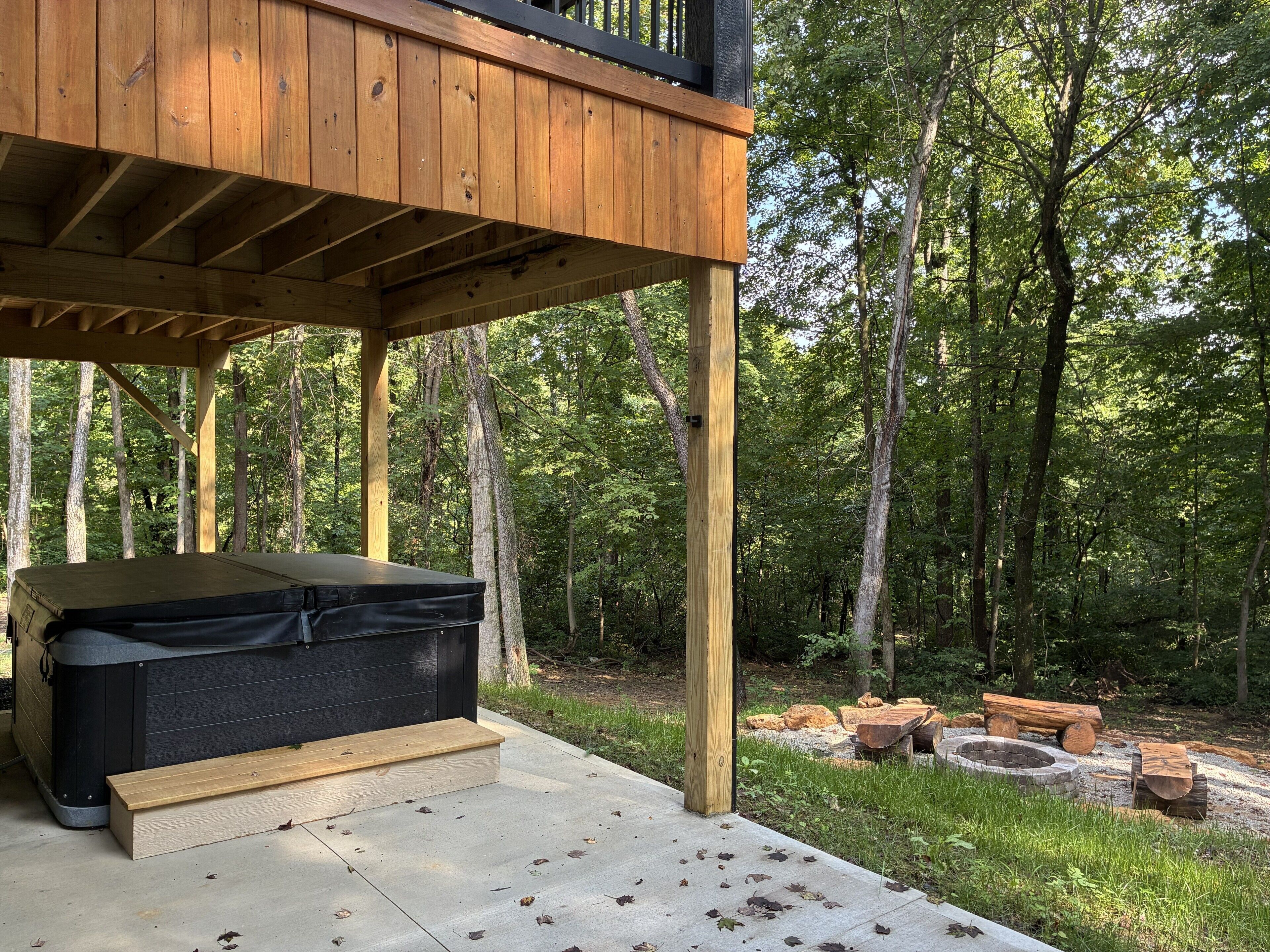 A wooden deck with a hot tub, a fire pit, and a stone fire pit.