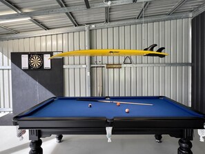 A pool table with billiard balls and cues, a dartboard, and a yellow object hanging above.