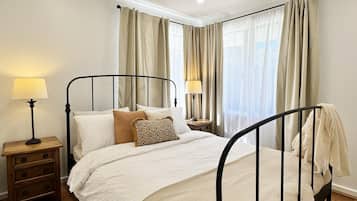 A bedroom with a four-poster bed, two bedside tables, and a window with curtains.