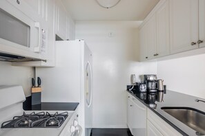A compact kitchen with a gas stove, white cabinets, a microwave, and a coffee maker. - Blueground | Kips Bay, pool, nr Empire State (New York)