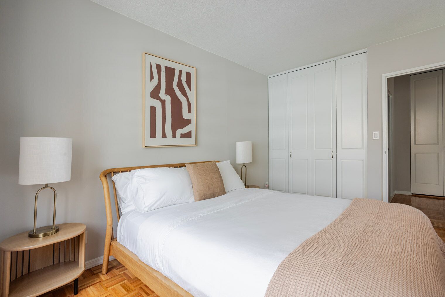 Ein Schlafzimmer mit einem Bett, Nachttischlampen, einem Kleiderschrank und einem gerahmten, abstrakten Kunstwerk an der Wand.