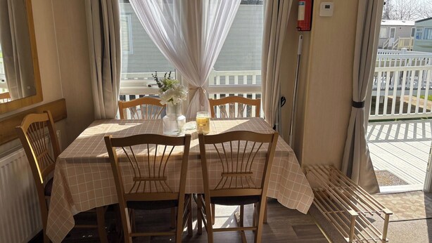 Un comedor con una mesa dispuesta para cuatro personas, sillas de madera, un florero con flores y una botella de jugo.
