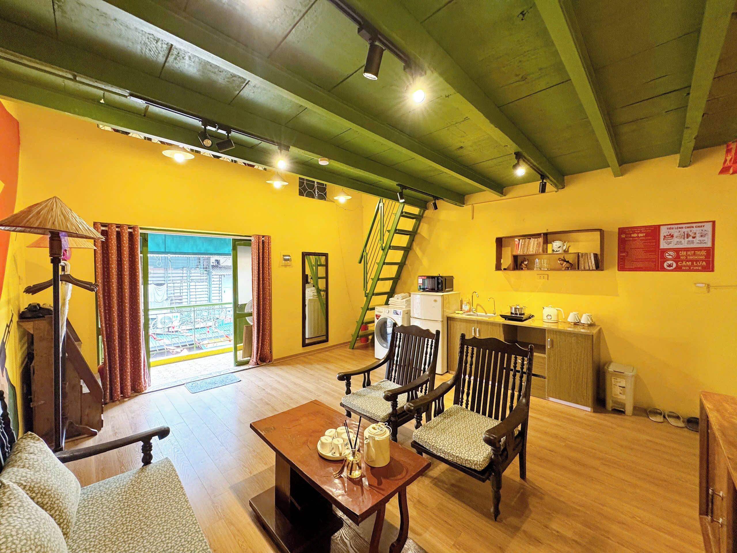 A room with a wooden floor, a dining table with chairs, a washing machine, a kitchen area with a sink and stove, and a staircase.