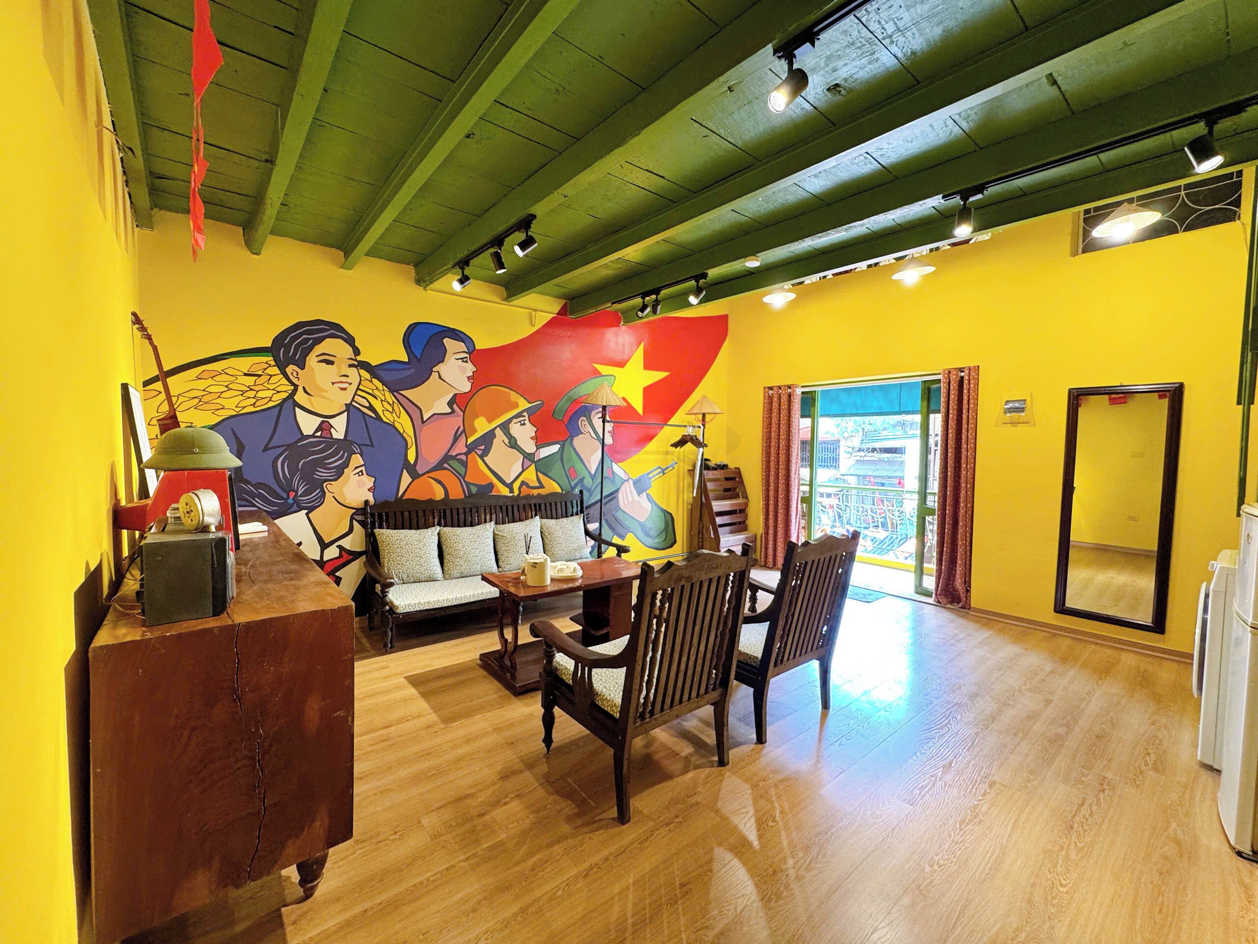 A room with a wooden floor, a sofa, a dining table with chairs, a mural on the wall, and a window with curtains.