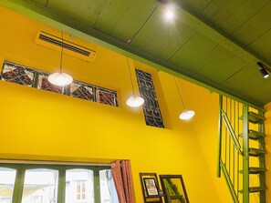 A room with yellow walls, a green ceiling, and a window with curtains. There is a ladder against the wall and a framed picture on the window sill. - Night Market View Apartment, Inside Walking Street, Large Balcony, Max 5 (Hà Nội)