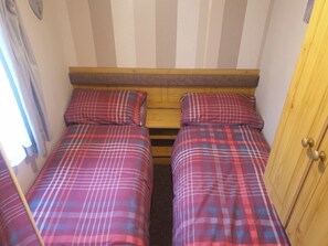 A small, compact room with two beds, each with a plaid bedspread and matching pillows. The room has a wooden headboard and a door on the right side. - 8 Berth caravan Butlins Skegness Pet friendly (Skegness)