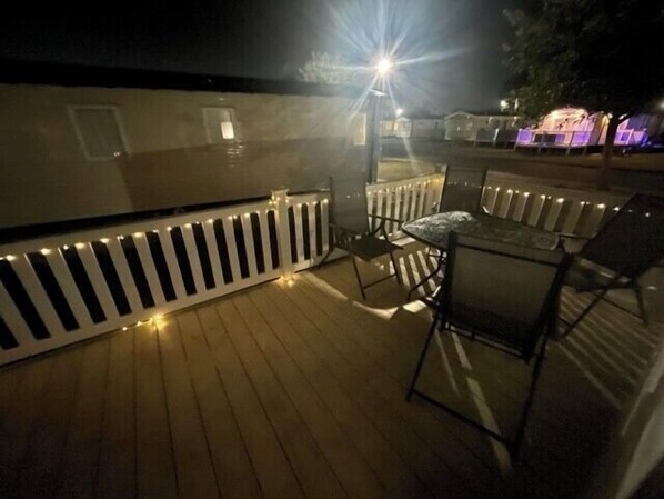 Una terraza de madera con barandilla, una mesa y sillas.