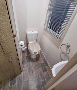 A small bathroom with a toilet, a bidet, and a window with blinds. - 8 Berth caravan Butlins Skegness (Skegness)