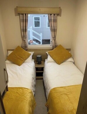 A small room with two beds, a window with curtains, and a view of a building outside. - 8 Berth caravan Butlins Skegness (Skegness)