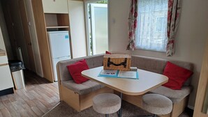 Ein gemütlicher, kleiner Wohnbereich mit Küchenzeile, einer Couch mit roten Kissen, einem kleinen Tisch und einem Korbwannenstuhl.