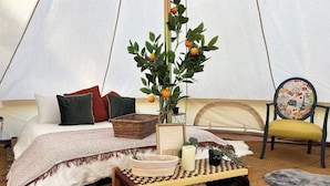 A tented accommodation with a bed, pillows, a table with a candle, a chair, and a plant with fruit. - Countryside Avon Escape for Two (Pewsey)