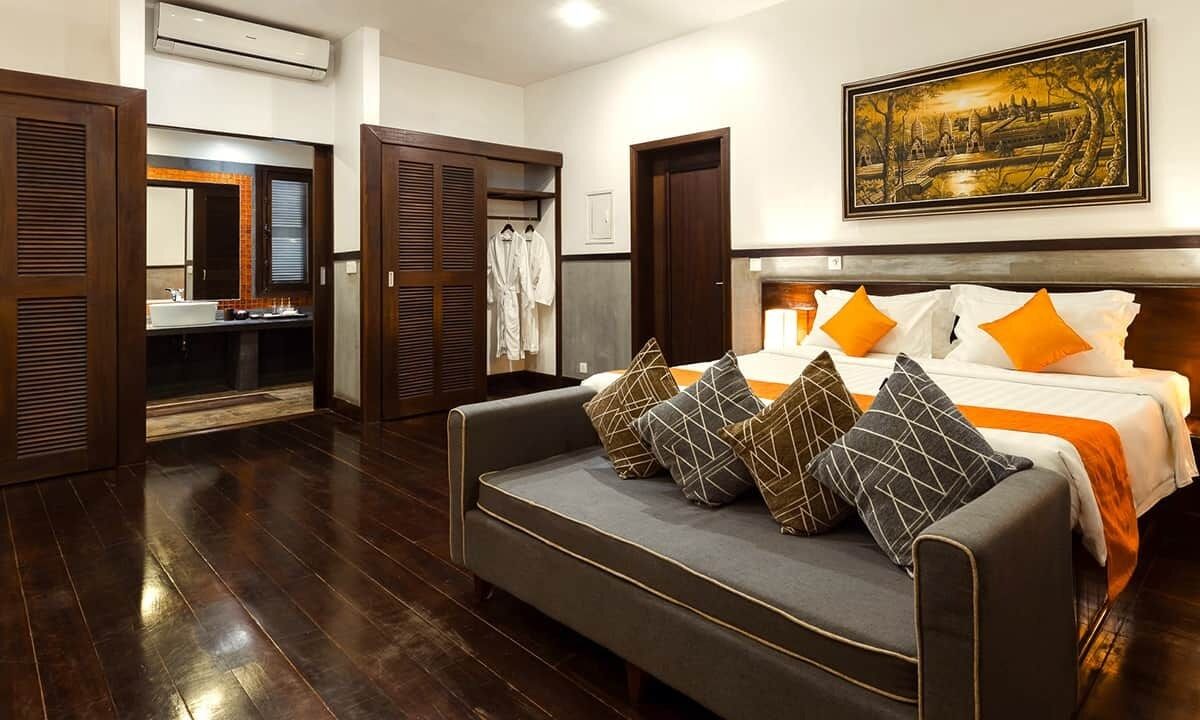 A hotel room with a bed, a sofa, a bathroom with a mirror, and a painting on the wall.
