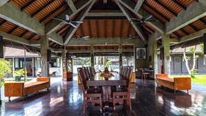 A spacious indoor area with a high ceiling, a central dining table surrounded by chairs, and a ceiling fan.