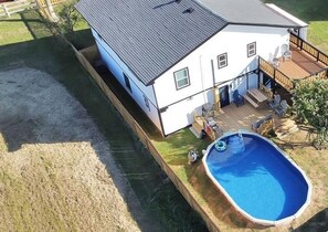 Ein zweistöckiges Haus mit einer Terrasse, einem Schwimmbecken und einem umzäunten Garten.