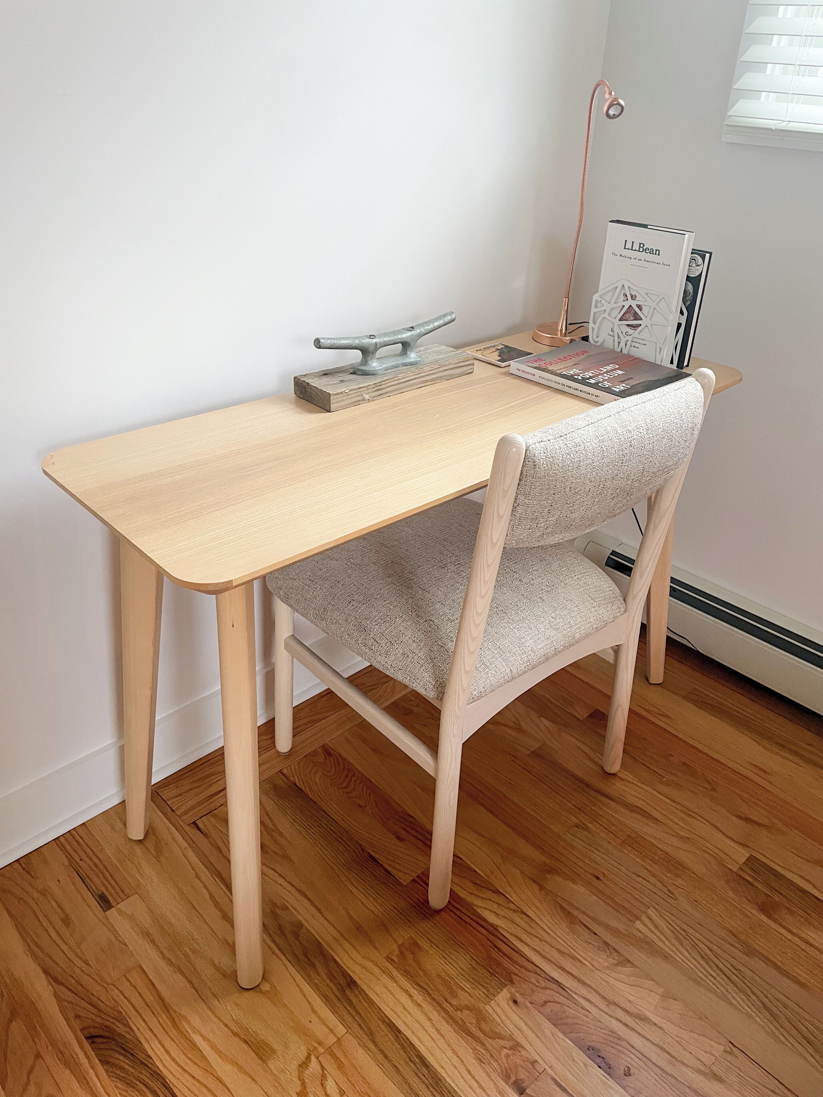 Uma mesa de madeira com uma cadeira, um livro intitulado 'L.L.Bean' e um objeto decorativo de metal sobre a mesa.
