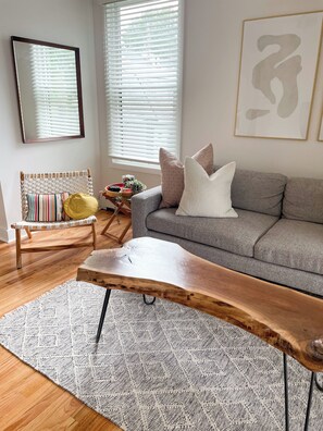 A living room with a grey sofa, a wooden coffee table, a woven chair, and a patterned rug. - Modern Retreat in East Bayside - walk to it all! (Portland)
