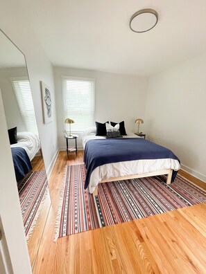 Een slaapkamer met een bed, een spiegel, een raam en een kamerkleed met een patroon.
