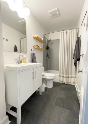 Een moderne badkamer met een wit wastafelmeubel, toilet, douche met gordijn en een spiegel.