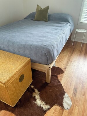 A bed with a grey bedspread, a green pillow, and a wicker storage box on a wooden floor. - Modern Retreat in East Bayside - walk to it all! (Portland)