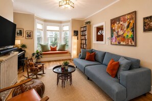 Ein Wohnzimmer mit einer Couch, einem Fernseher, einem Bücherregal und einem Gemälde.