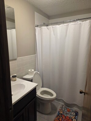 Un baño con inodoro, lavamanos, espejo y cortina de ducha.